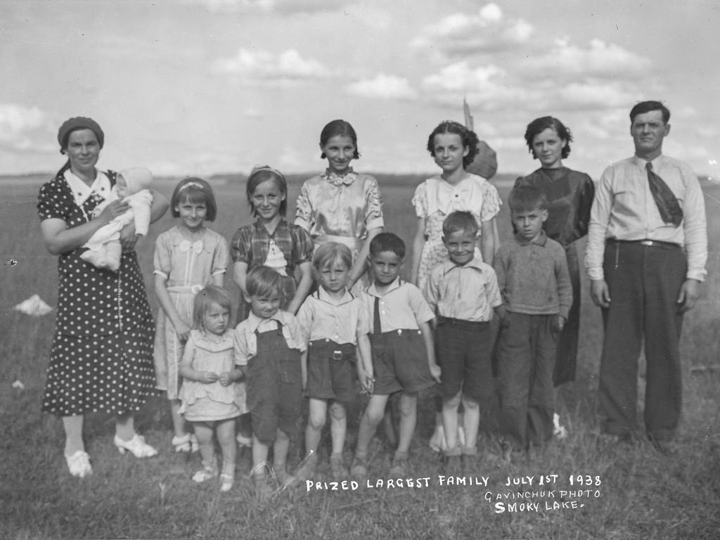 Photo of family standing in field, caption reads "Prized largest family, July 1st 1938, Gavinchuk Photo, Smoky Lake" - PAA photo # G402